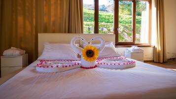 A neatly made bed with white linens, a heart-shaped towel arrangement, and a sunflower centerpiece.