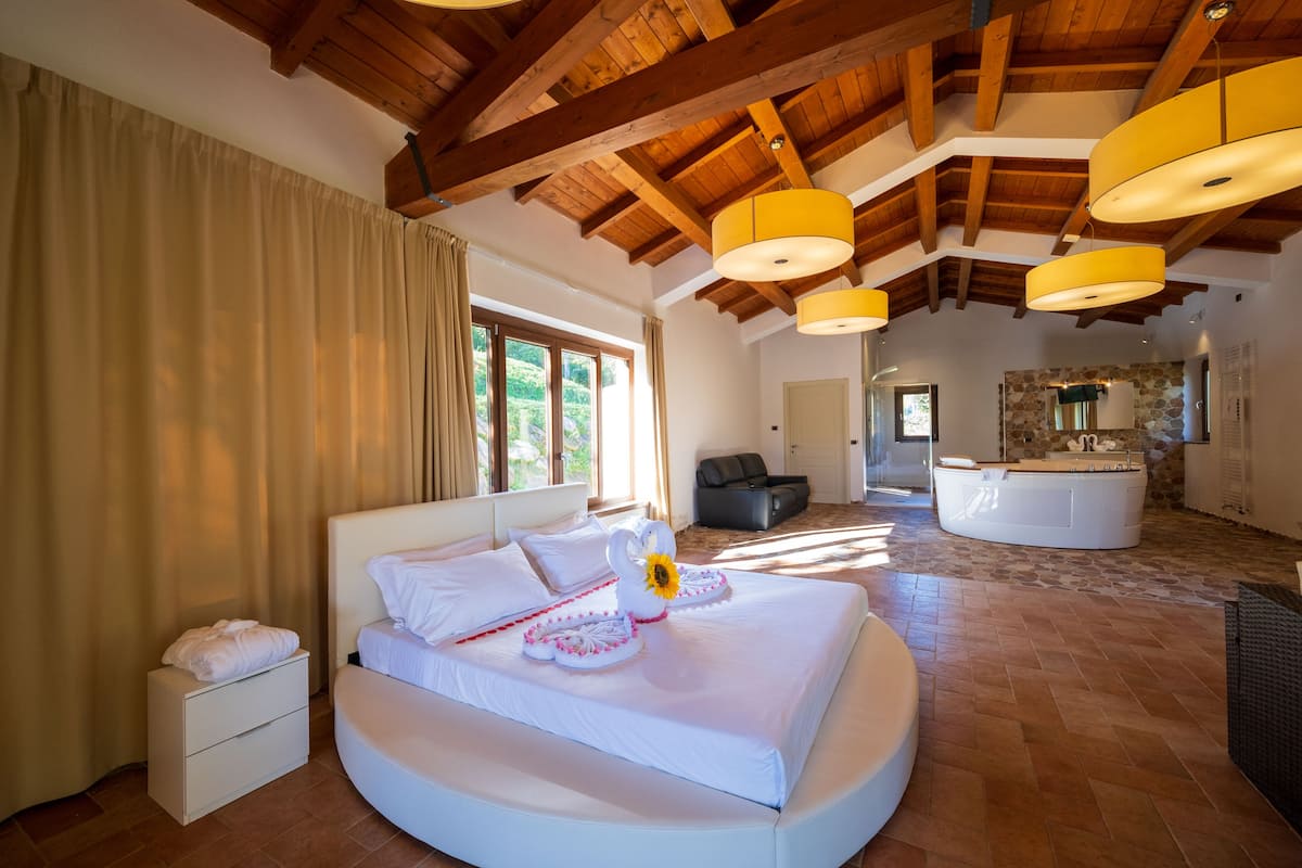 Un dormitorio espacioso con una cama grande, techo de madera y pared de piedra al fondo.