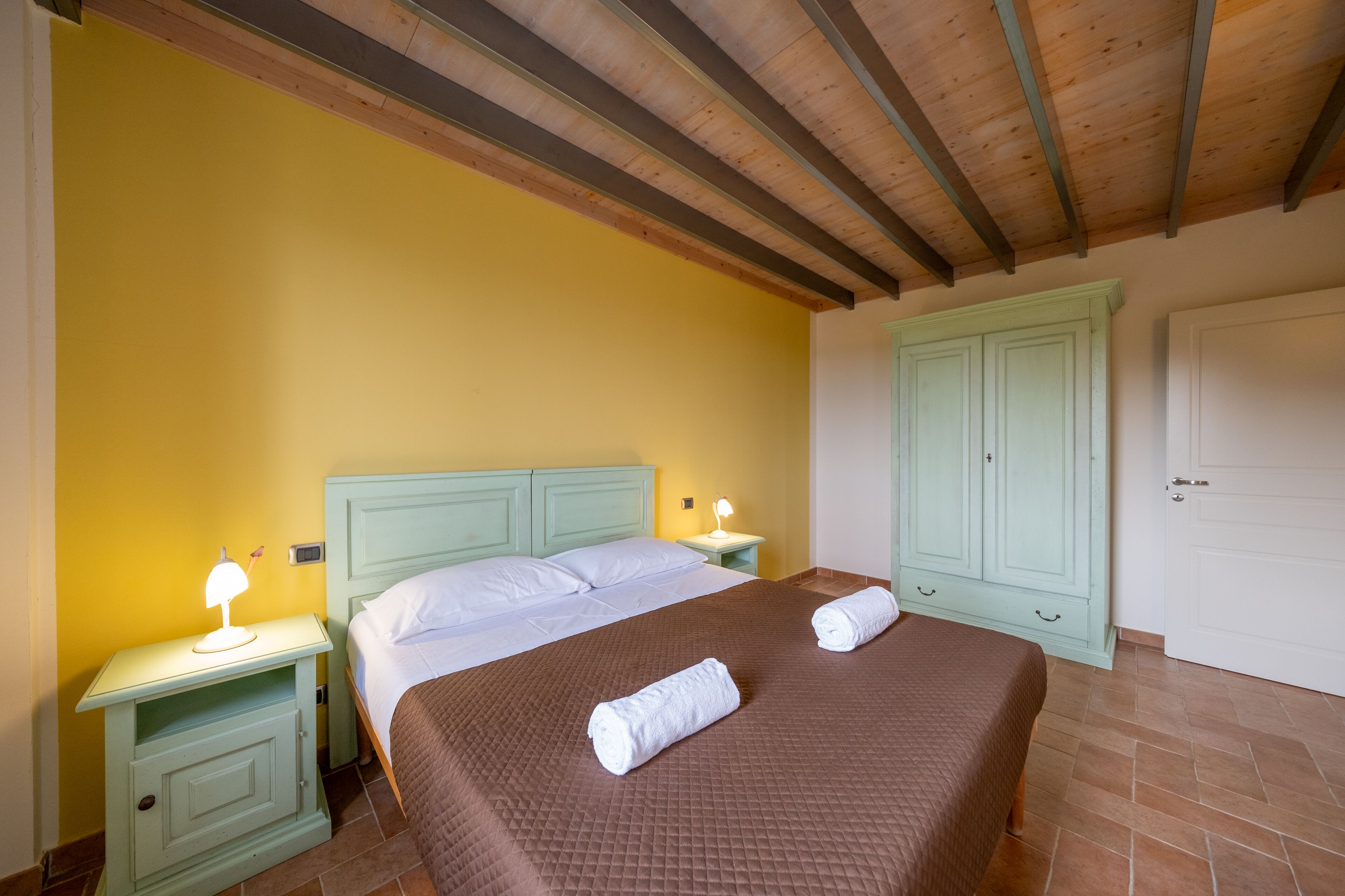 Een slaapkamer met een bed, twee nachtkastjes, een kledingkast en een deur.
