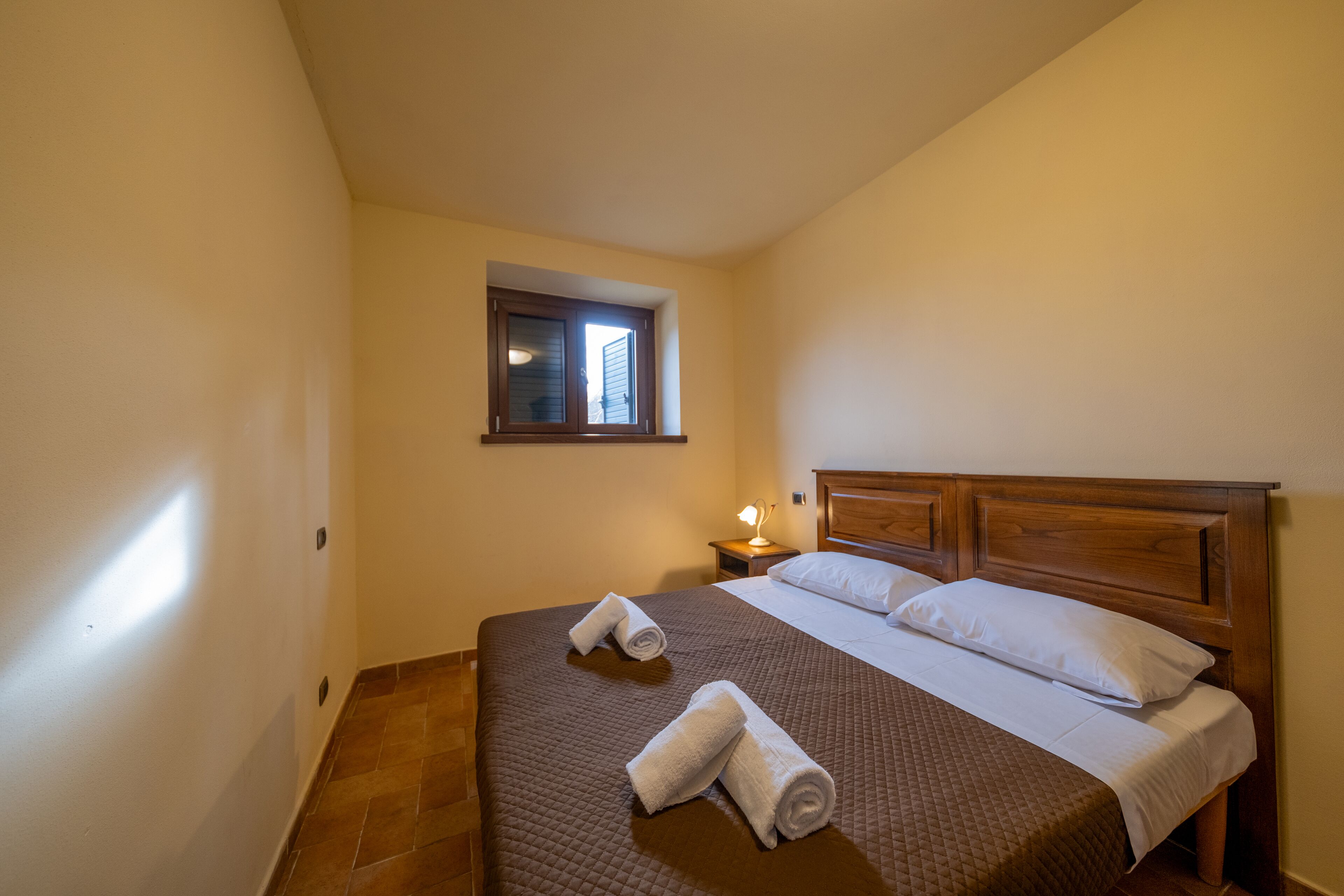 Ein Schlafzimmer mit einem Bett, zwei Kissen, einem Nachttisch mit einer Lampe und zwei aufgerollten Handtüchern.