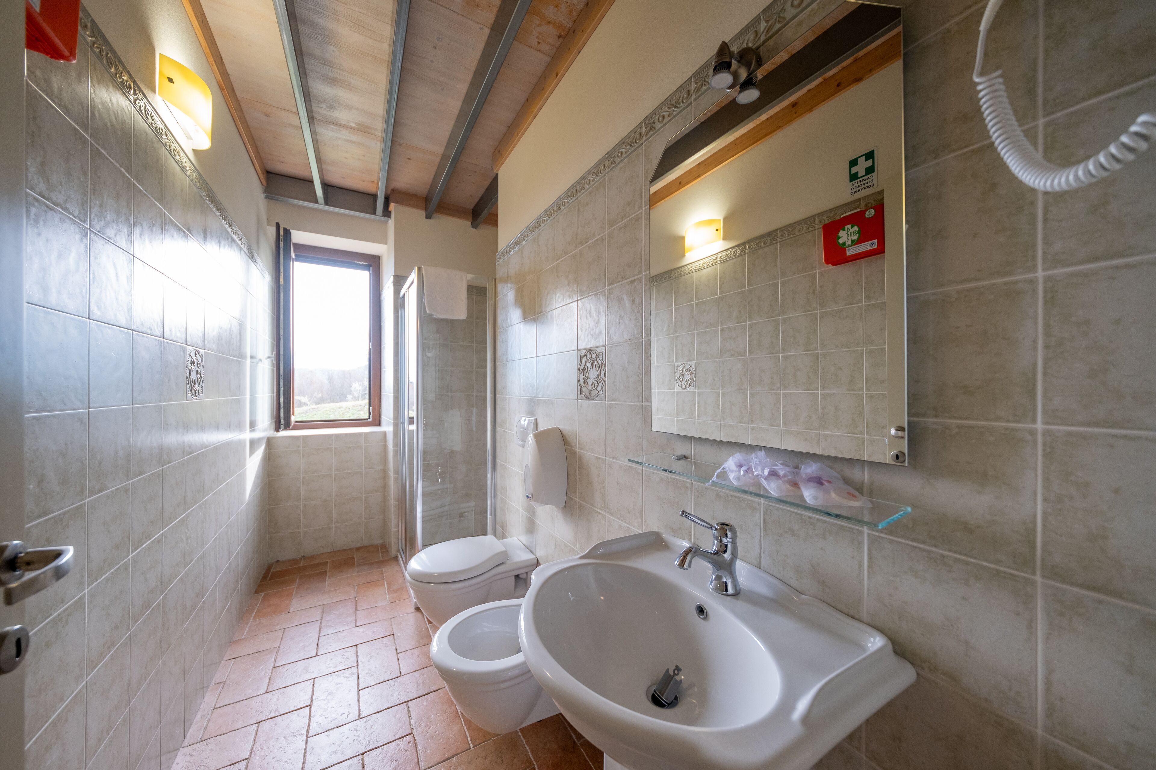 Un baño con dos inodoros, un lavabo, un estante de vidrio y una ventana.