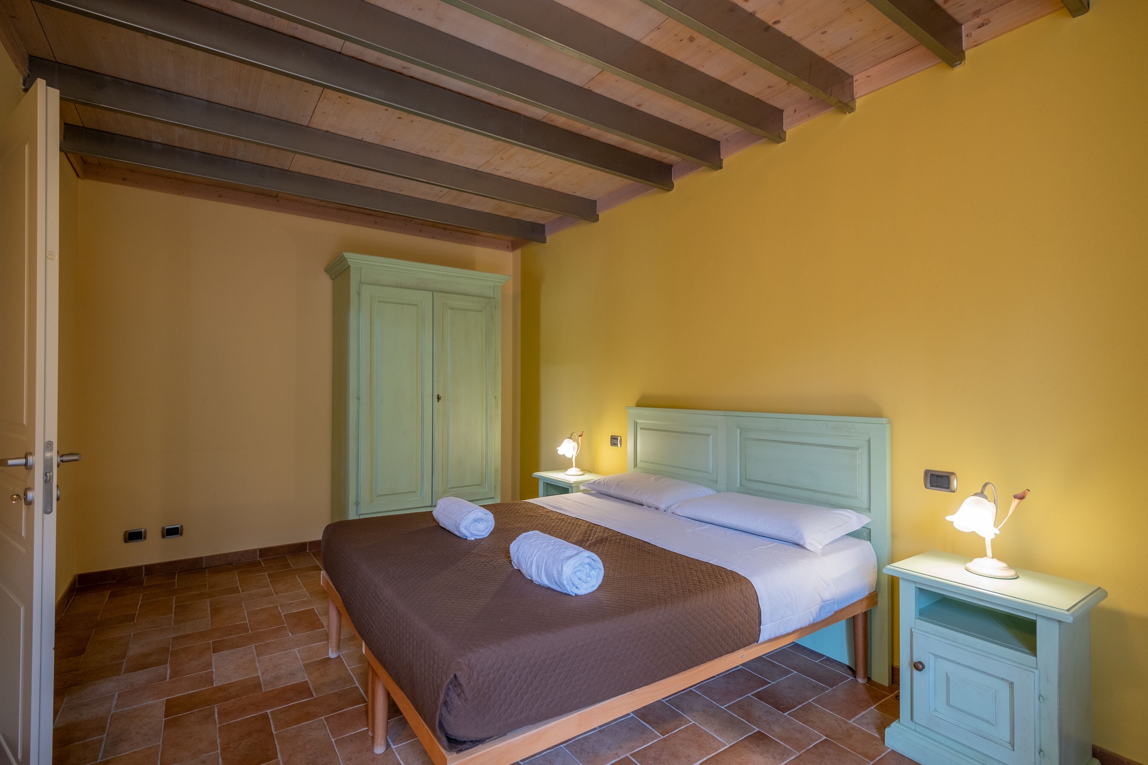 A bedroom with a bed, two bedside tables with lamps, a wardrobe, and a door.