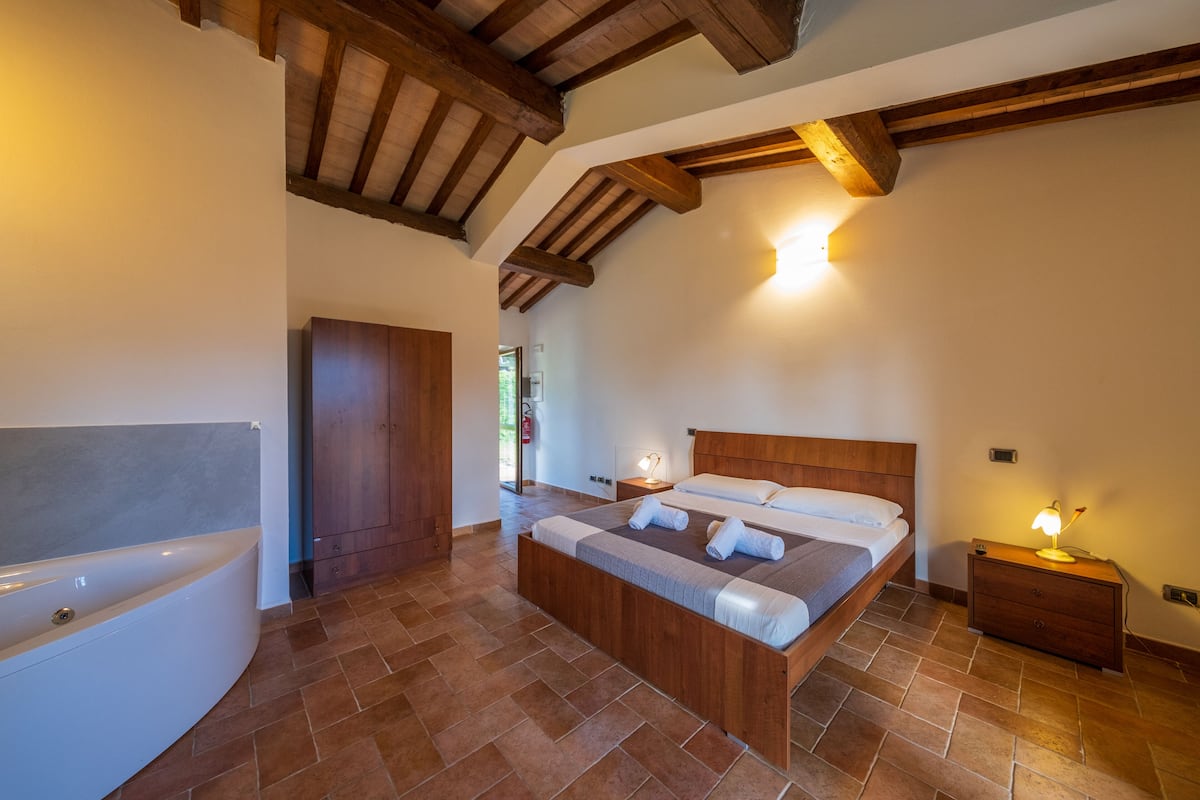 Un dormitorio con una cama de madera, una mesita de noche con lámpara, un armario de madera y un baño con bañera.