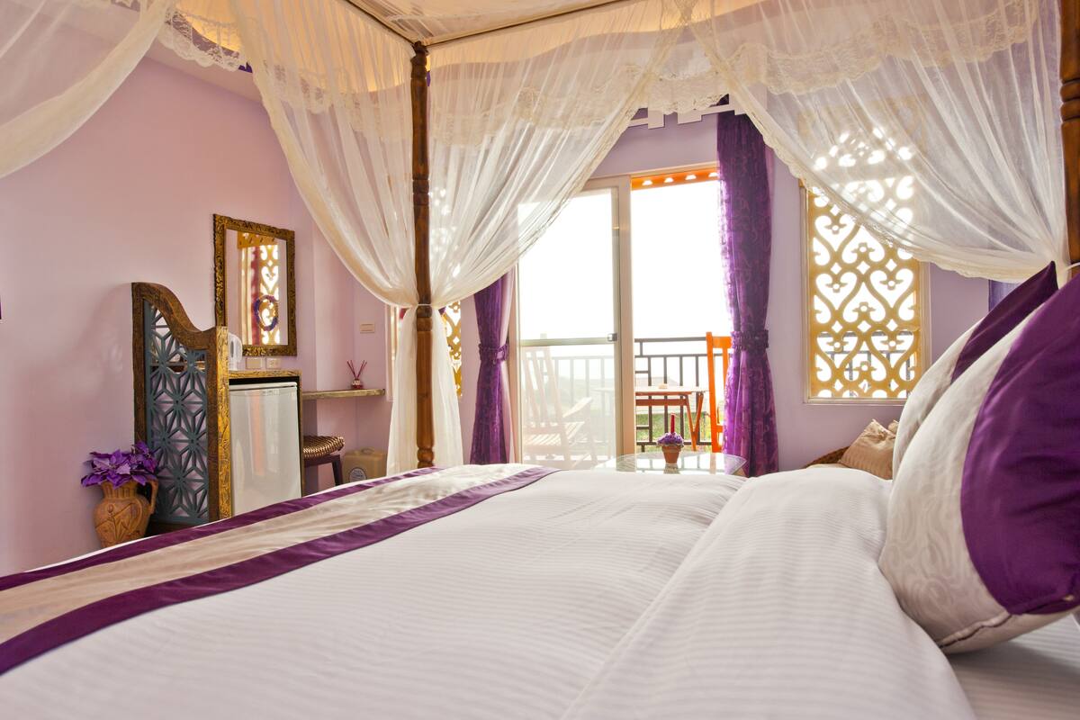 Un dormitorio con cama, mesita de noche, espejo y ventana con cortinas.