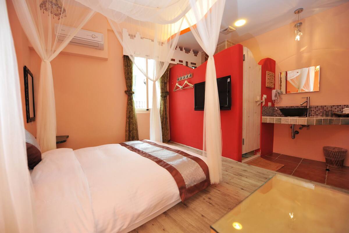 Un dormitorio con cama, espejo, lavamanos y una pared de acento roja.