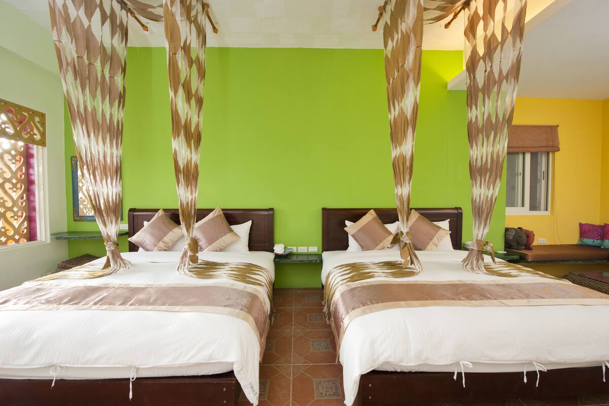 Habitación de hotel con dos camas, paredes verdes y una ventana con cortina marrón.