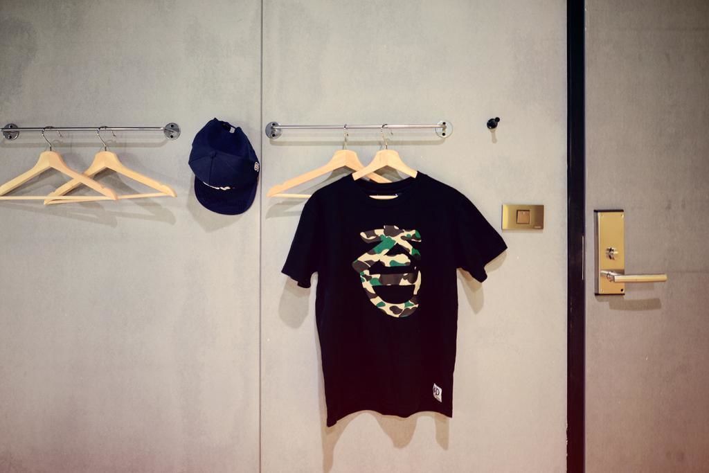 A room with a door, a coat rack with hangers, and a black t-shirt with a camouflage design on the wall.