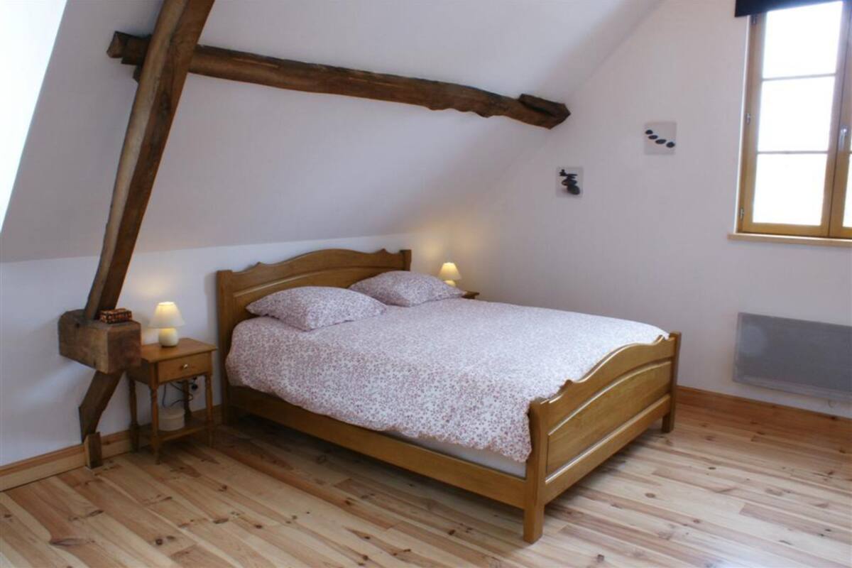 A bedroom with a wooden bed, two bedside tables with lamps, a slanted ceiling, and a window.
