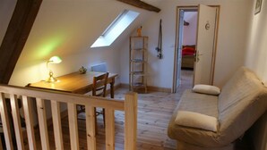 Une chambre mansardée chaleureuse avec un plafond en pente, un bureau en bois avec une lampe, un banc rembourré et une échelle.