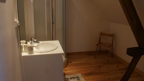 Une petite salle de bain avec un lavabo blanc, un miroir et une chaise en bois.