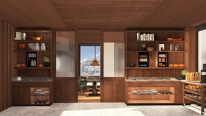 A modern kitchen with wooden cabinetry, a view of a snowy landscape, and various kitchen appliances and utensils. - New Hotel Kristberg in Lech with Spa, outdoor pool and panoramic view (Lech am Arlberg)