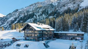A modern ski resort with a large lodge featuring multiple floors and large windows, surrounded by snow-covered mountains and trees. - New Hotel Kristberg in Lech with Spa, outdoor pool and panoramic view (Lech am Arlberg)