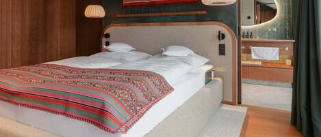 A modern hotel room with a large bed, a wooden ceiling, a bathroom with a mirror, and a green wall.