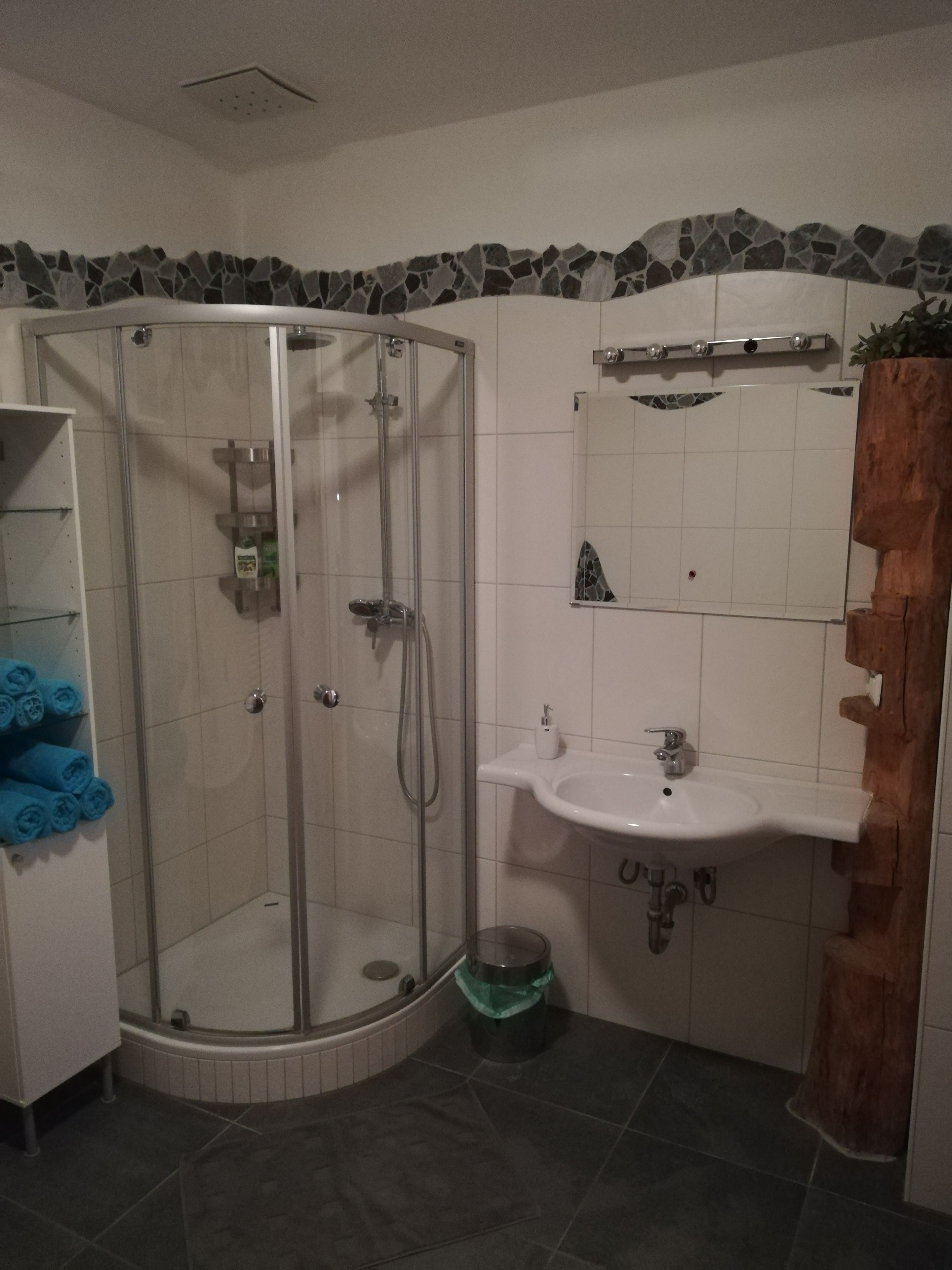 A bathroom with a glass shower enclosure, a white sink, and a wooden accent wall.