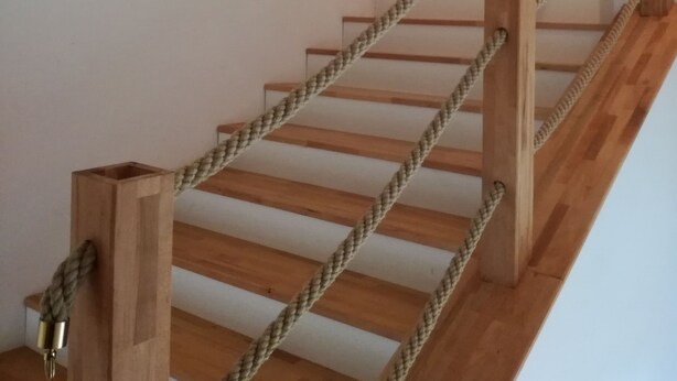 A wooden staircase with rope handrails, white walls, and a wooden door at the top.