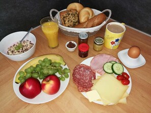 Een ontbijttafel met diverse etenswaren zoals brood, fruit, kaas, ham en een kop koffie.
