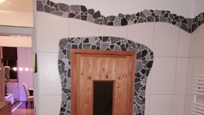 A bathroom with a stone mosaic wall, a wooden door, and a white tiled floor.