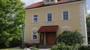 A two-story building with a red-tiled roof, a central entrance with a red awning, and a small upper balcony.