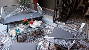 A patio area with two metal chairs with cushions, a small table with a tray of items, and a potted plant. - Athenian Yard Suites (Athens)