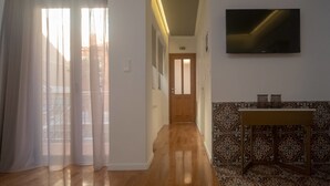 A hallway with a wooden floor, a patterned wall, a television mounted on the wall, and a door at the end. - Athenian Yard Suites (Athens)