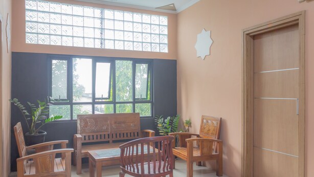 Una habitación con un juego de sofá de madera, una mesa de comedor y sillas. Amplias ventanas ofrecen vista a zonas verdes.