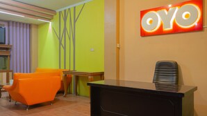 Zona de recepción con un mostrador negro, una silla naranja, una mesa de madera y una pared con el letrero 'OYO'.
