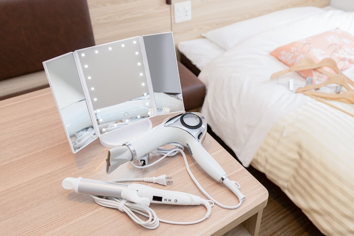 A neatly arranged hotel room with a vanity mirror, a hairdryer, and a charging station on a wooden nightstand.