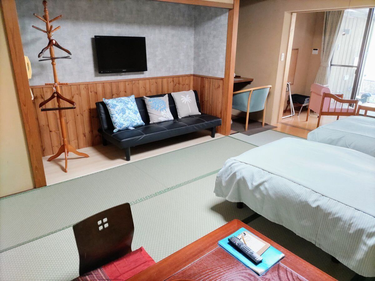 Una habitación de hotel con cama, sofá, televisor y perchero de madera.