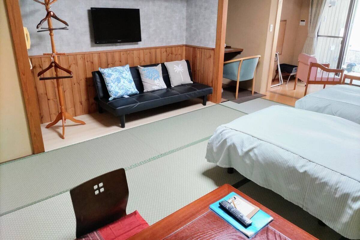 Quarto de hotel com uma cama, um sofá, uma televisão e um porta-roupas de madeira.