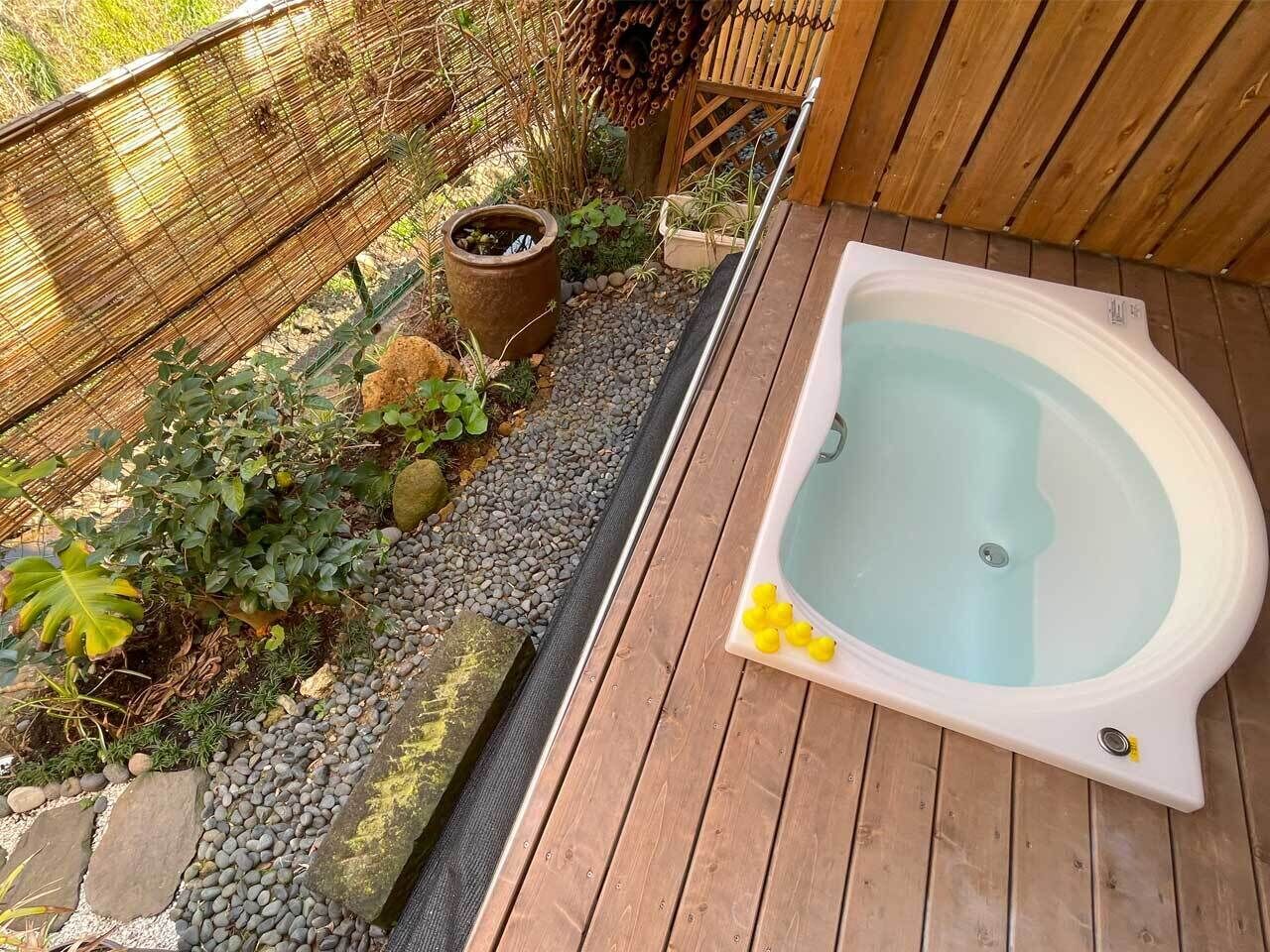 A hot tub on a wooden deck with a garden area featuring plants and a bamboo fence.