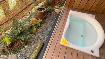 A hot tub on a wooden deck with a garden area featuring plants and a bamboo fence.