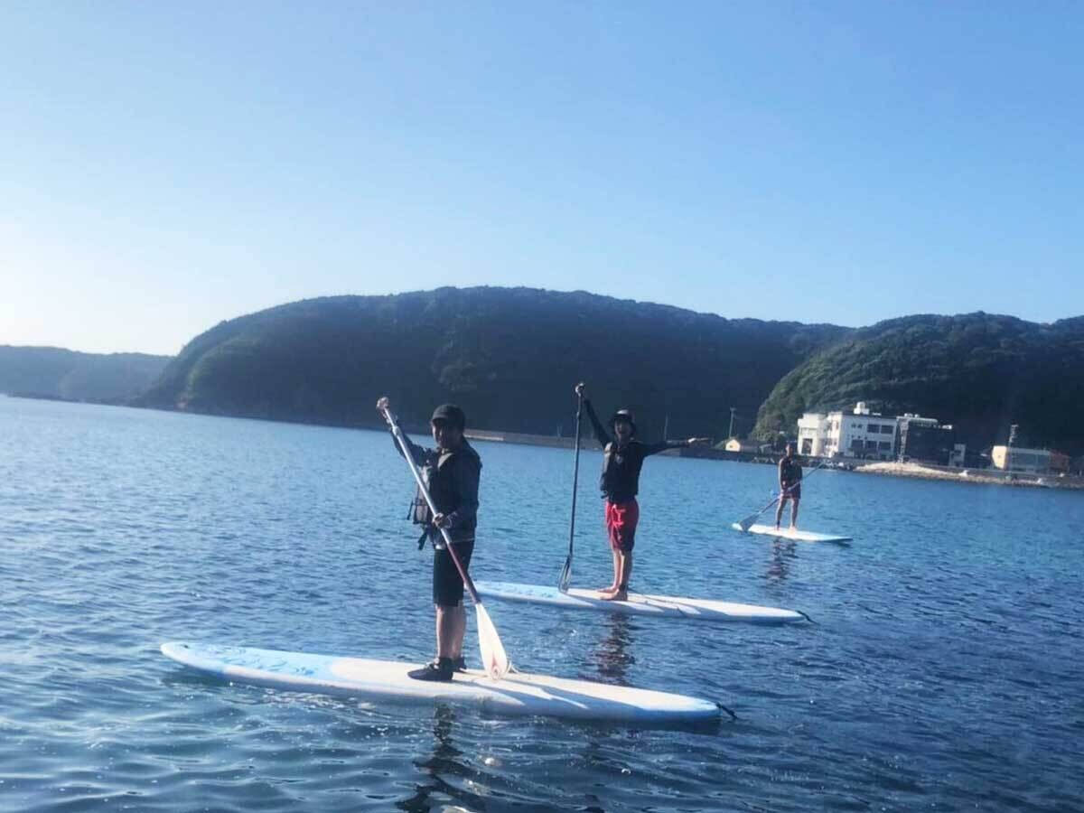 Three people stand-up paddleboarding on calm water with a hilly landscape in the background.