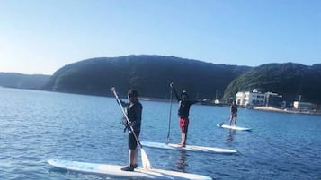 Three people stand-up paddleboarding on calm water with a hilly landscape in the background.
