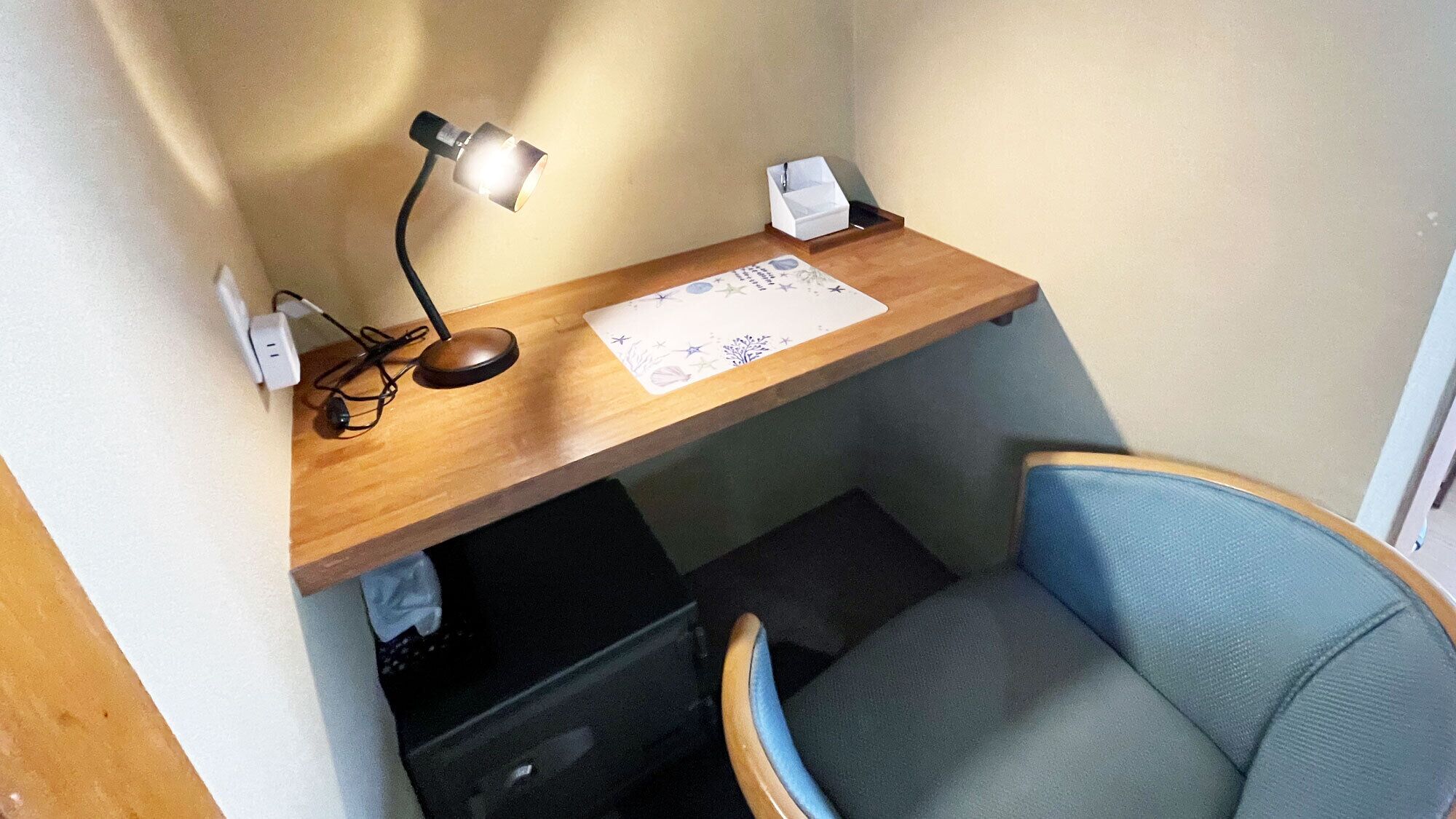 Un espacio de trabajo pequeño con un escritorio, una silla, una lámpara y un par de gafas.
