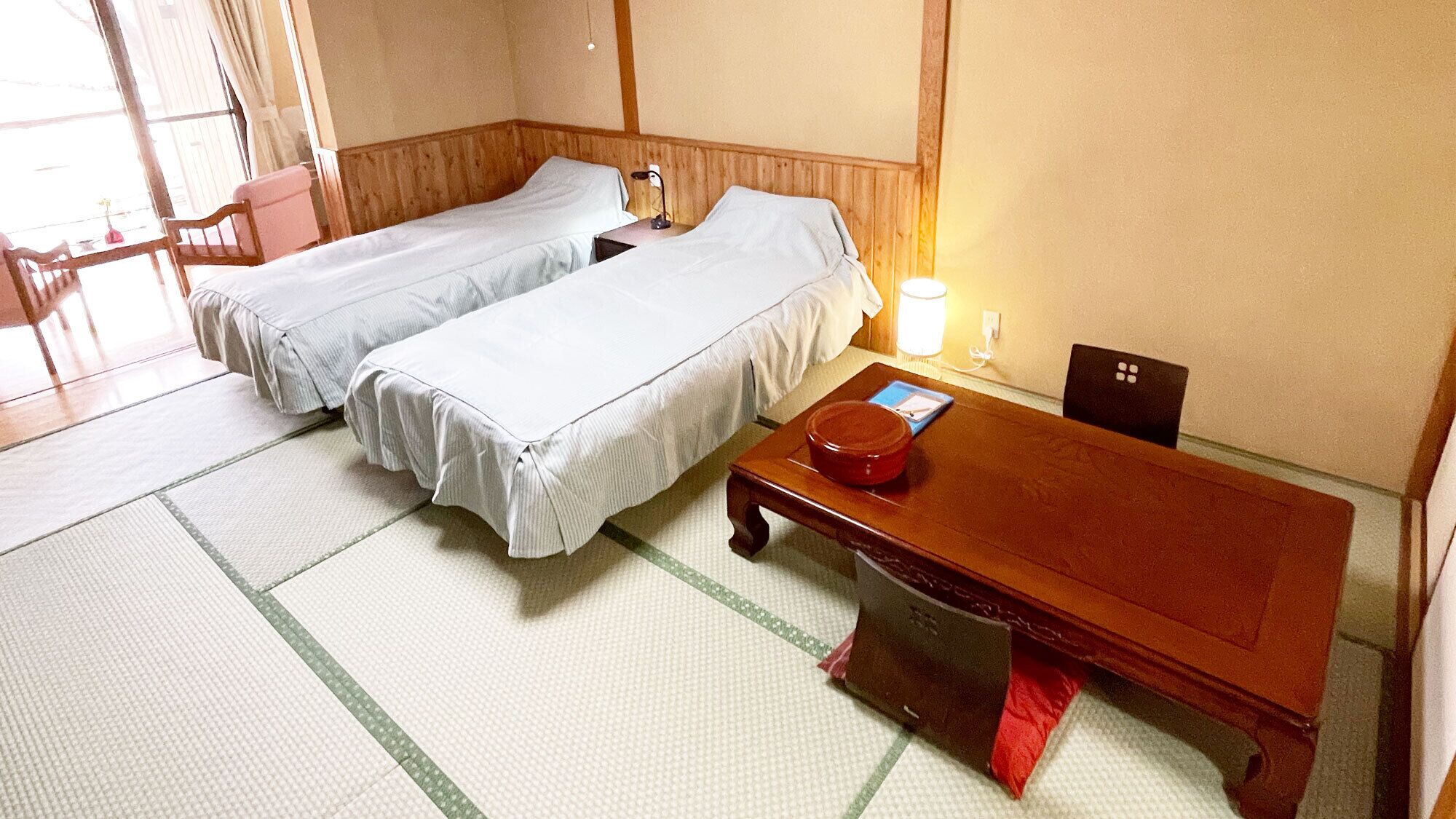 A traditional Japanese-style room with two single beds, a wooden table, and tatami flooring.