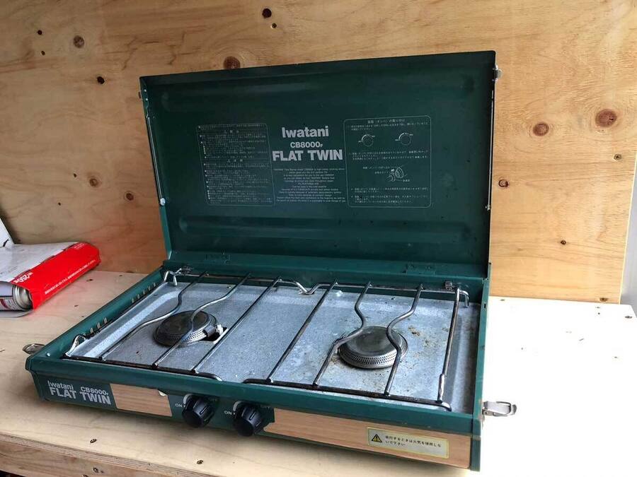 A portable flat twin stove with a green exterior and two burners, placed on a wooden surface.