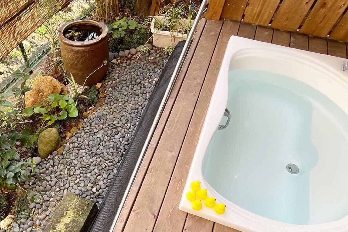 Um deck de madeira com hidromassagem e um pequeno jardim com plantas e um vaso.