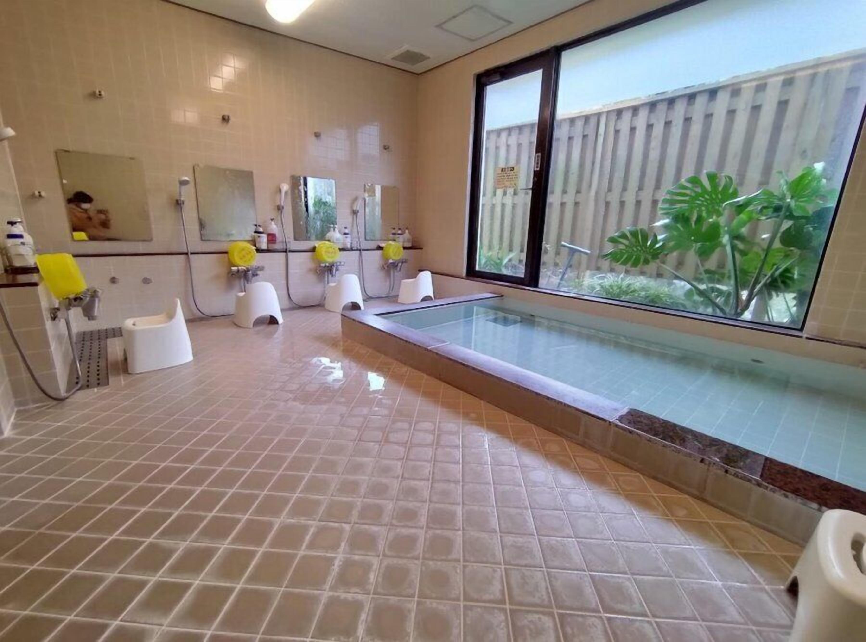A bathroom with a large window, a glass-enclosed pool, and multiple sinks with yellow soap dispensers.