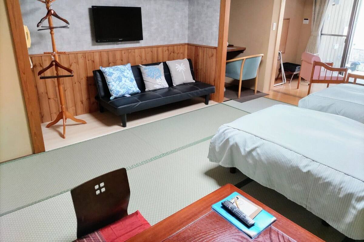 Quarto de hotel com cama, sofá, televisão, escrivaninha e cadeira.