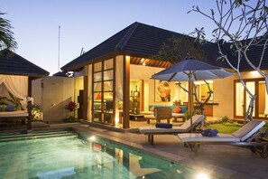 Ein Pool mit Liegestühlen und einem Sonnenschirm, ein Essbereich mit Tisch und Stühlen sowie ein großes Fenster mit Blick auf den Pool.