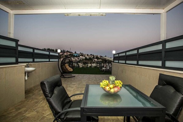 A balcony with a glass table, two black leather chairs, a hanging chair, and a bowl of fruit. - HApalmach 35 (Safed)
