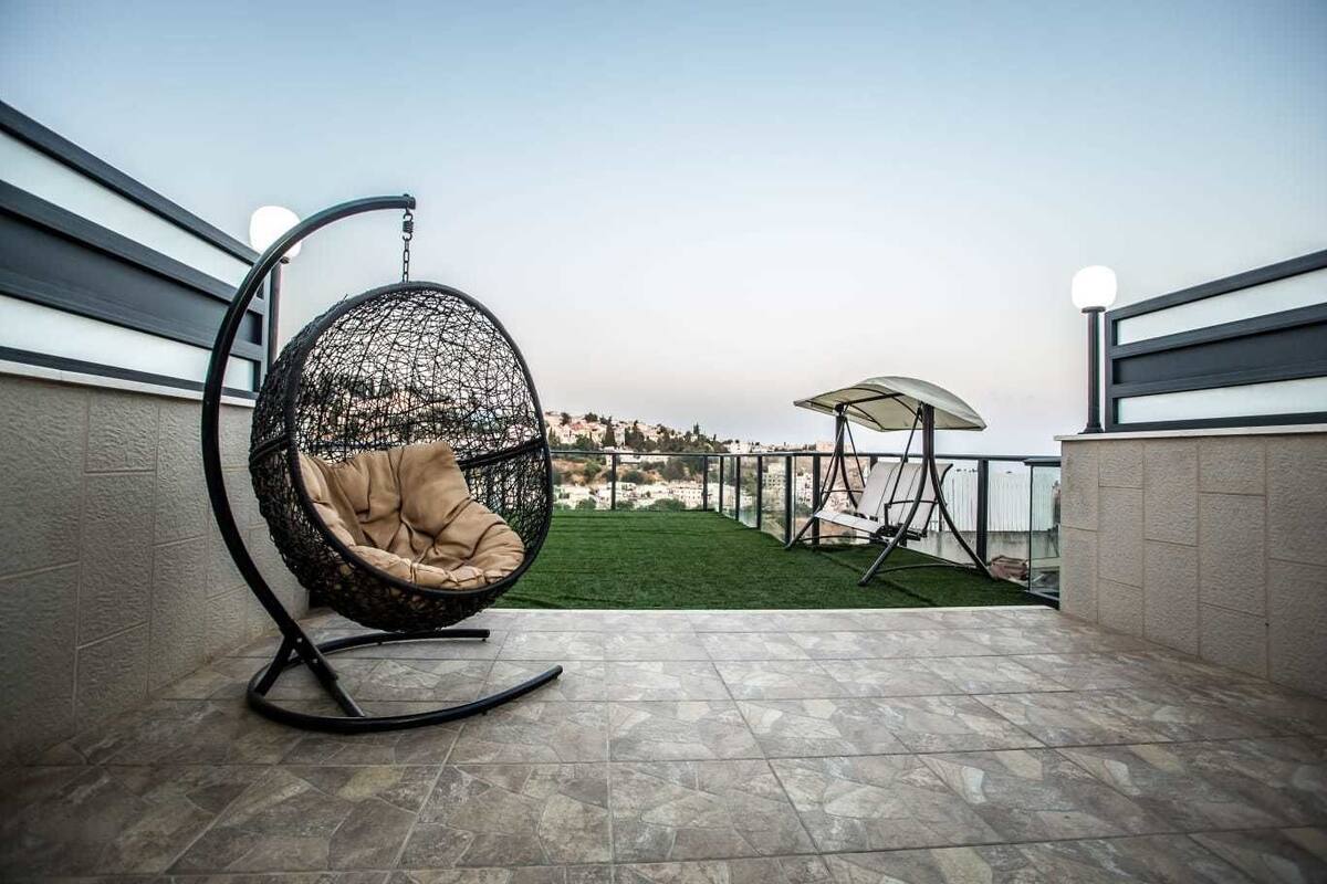 Un patio con una silla colgante, un columpio y vistas a un césped verde y edificios a lo lejos.