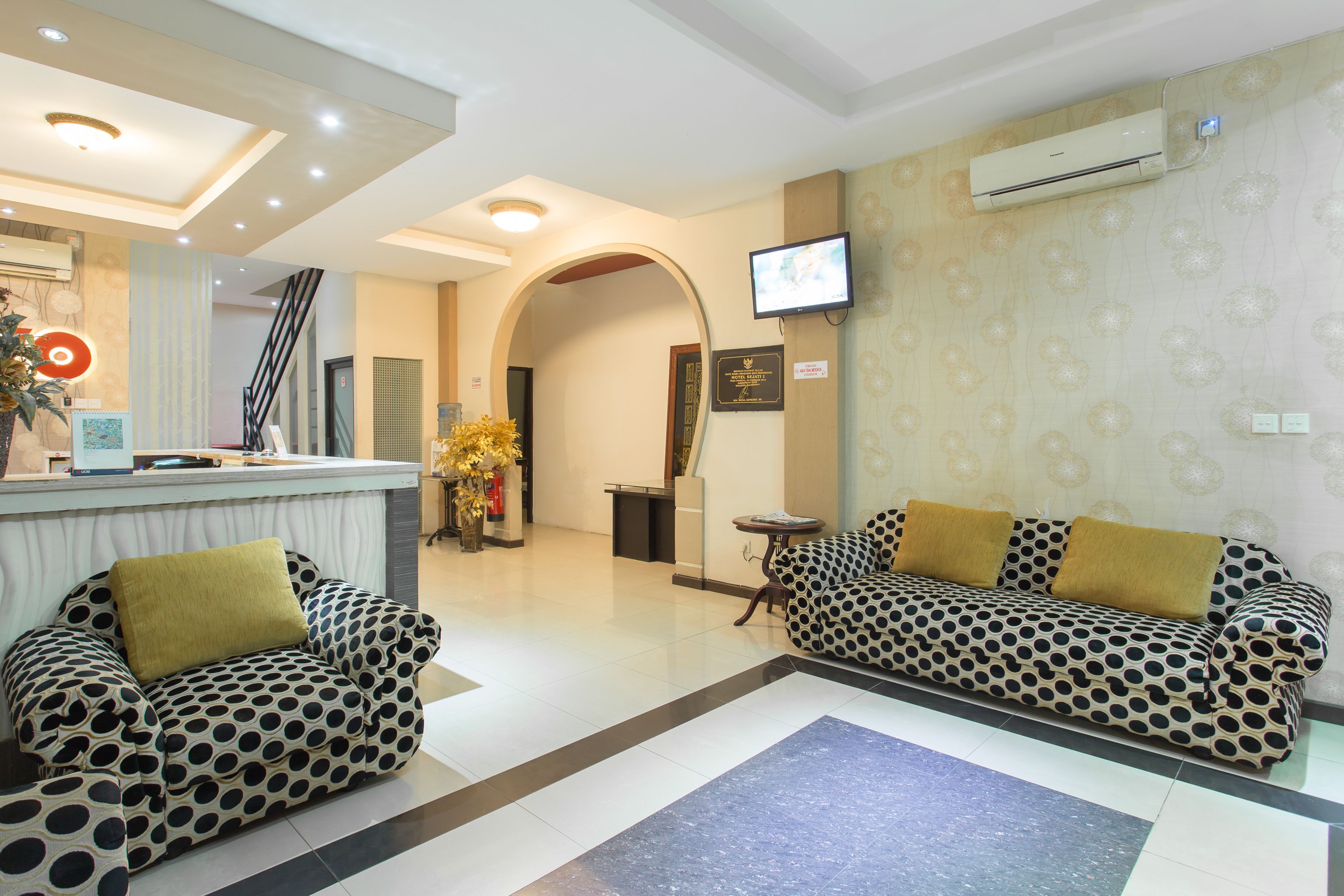 A reception area with a reception desk, two patterned sofas, a television, and a decorative plant.