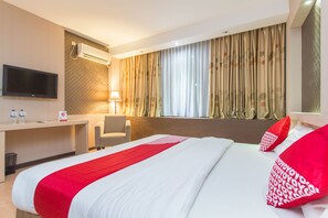 Une chambre d’hôtel avec un lit, un bureau, une chaise, une télévision et une fenêtre avec des rideaux.