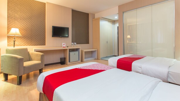 Ein Hotelzimmer mit zwei Betten, einem Schreibtisch, einem Sessel, einem Fernseher und einem Kleiderschrank.