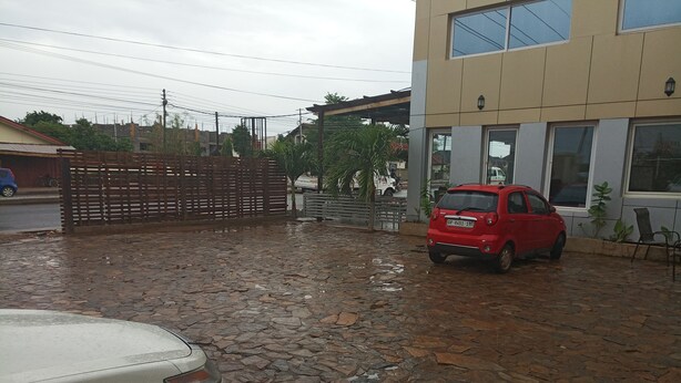 Un patio empedrado con un coche rojo estacionado frente a un edificio con grandes ventanales.