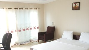Un dormitorio con una cama grande, un escritorio, una silla, un ventilador de techo y una ventana con cortinas.