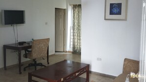Una sala de estar con televisor, una mesa de centro, dos sillones estampados, un cuadro en la pared y una puerta que da a otra habitación.