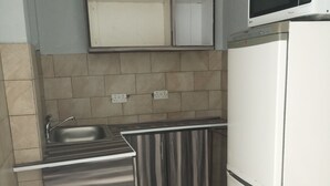 Una cocina compacta con un lavamanos de acero inoxidable, un refrigerador blanco y un microondas encima.