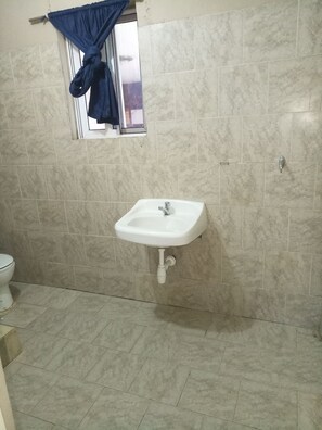 A bathroom with a white sink, a toilet, and a window with a blue curtain. - Ausbuild (Accra)